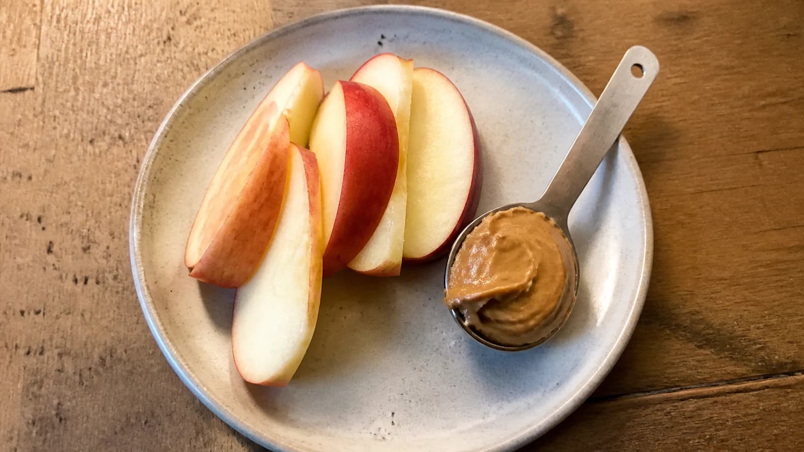 Half a red apple sliced beside one measured spoonful of unsweetened peanut butter