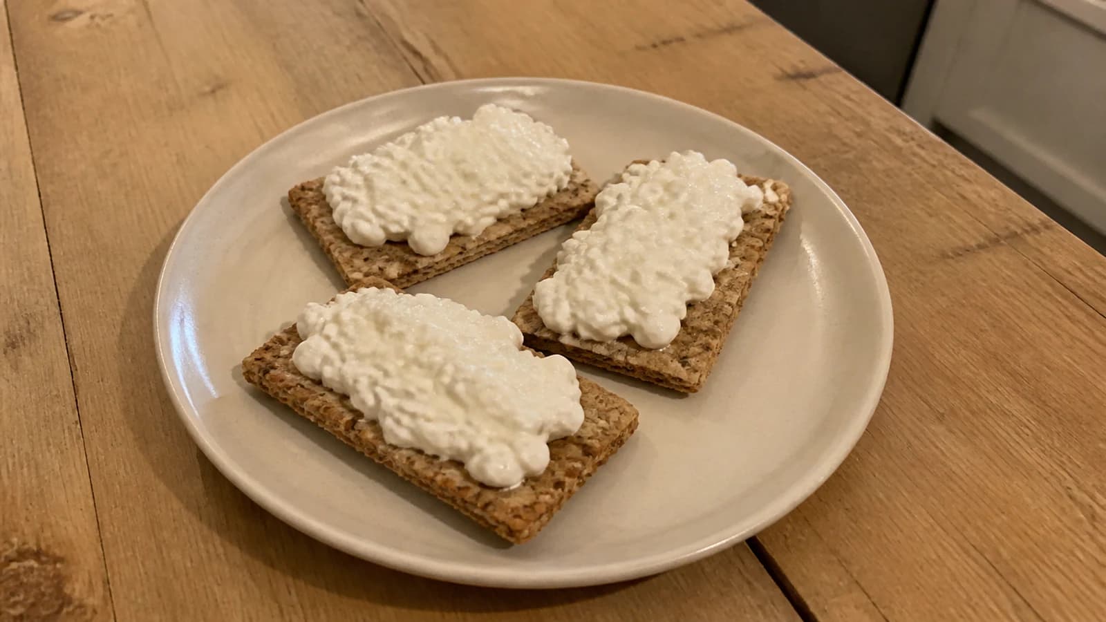 Three whole-grain crackers topped with plain cottage cheese on a ceramic plate