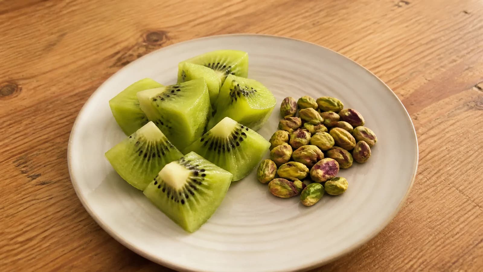 One ripe kiwi cut into pieces beside a small handful of unsalted shelled pistachios